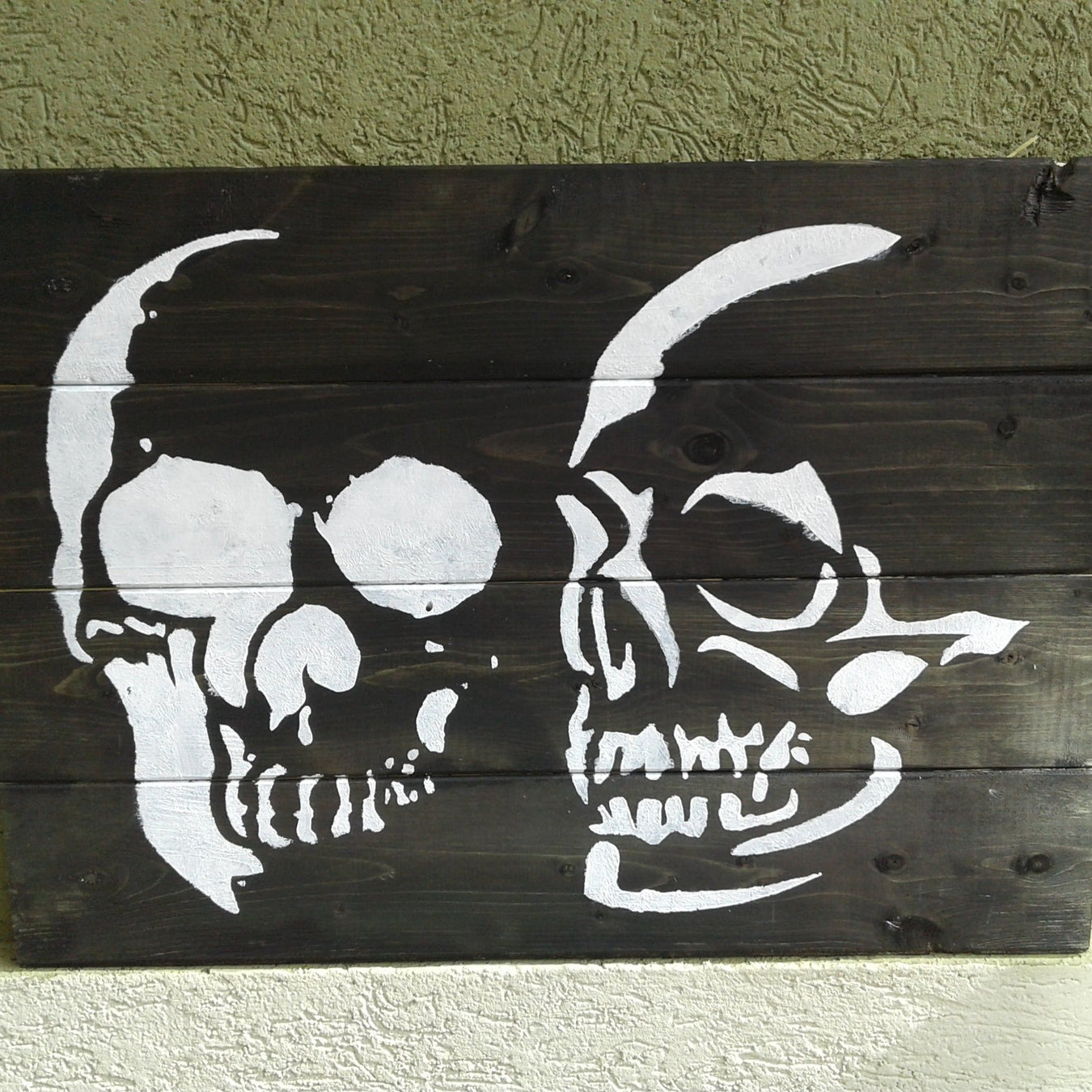 fron facing and side profile skull painted on dark wood using paint stencil