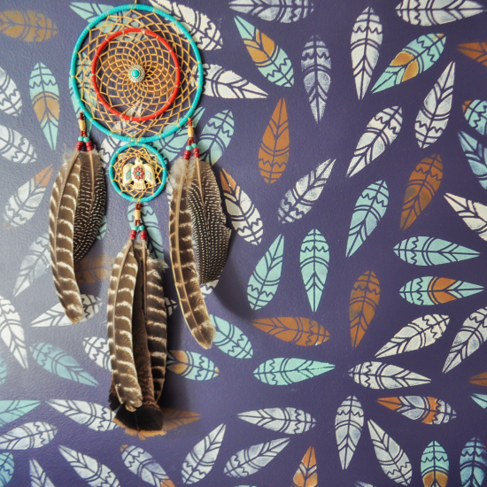 a dreamcatcher against a wall painted with Navajo tribal feathers using paint stencil